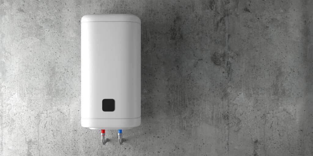Chauffe-eau mural blanc cylindrique installé sur un mur en béton brut. Raccords de plomberie rouge et bleu visibles en bas.